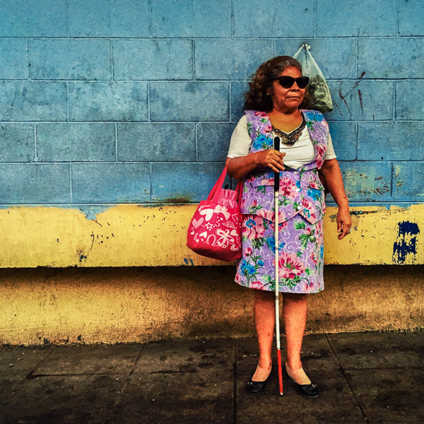 A blind woman, holding a white cane, waits for a bus in the backyard of San Miguelito public market in San Salvador, El Salvador.