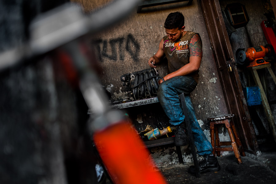 A Colombian car mechanic works on an engine in a car repair shop in Barrio Triste, Medellín, Colombia.