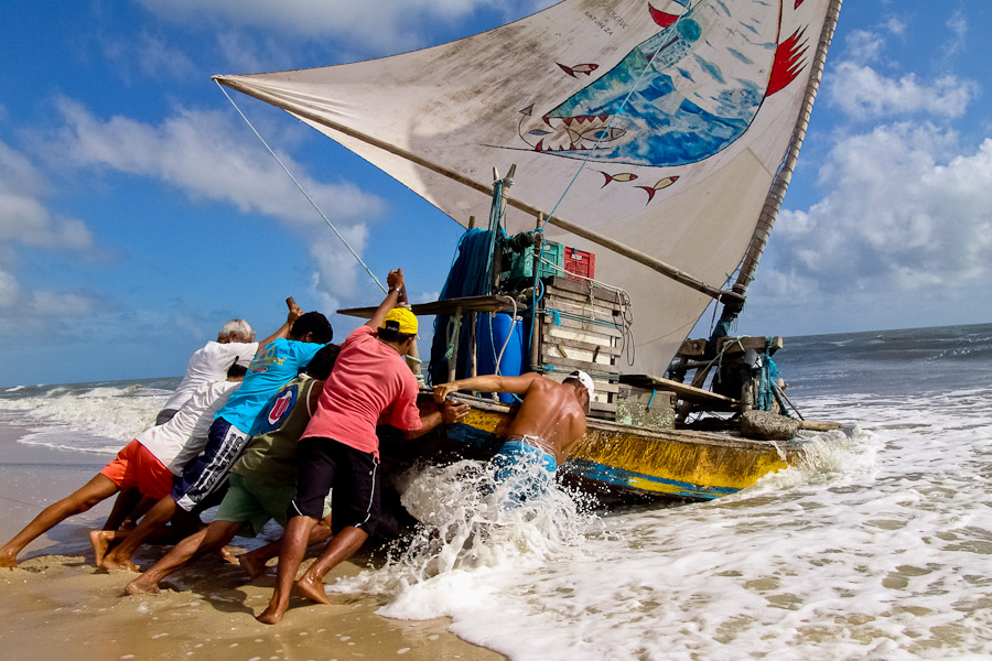 Jangadeiros move the boat towards the sea using wooden logs. Jangada has an unfixed keel and a mast that make it practical for a use on the shallow sea and beaches of the nothern Brazil.