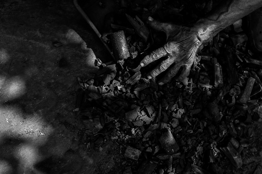 A hand of an Afro-Colombian charcoal worker, full of bulging veins, is seen scooping charcoal from the ground into a shovel in a street market in Barranquilla, Colombia.