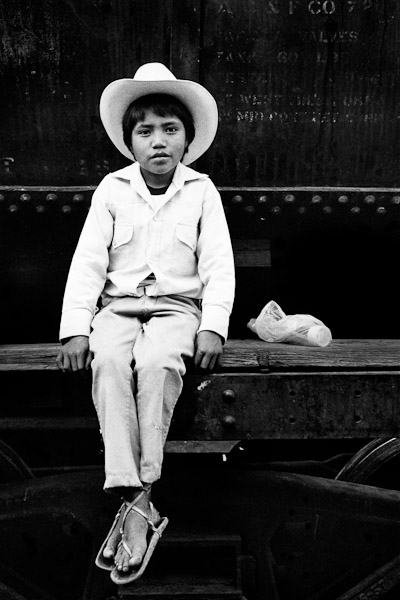 A Mexican boy, wearing white cowboy clothes, sits on the wagon of the legendary Chihuahua-Pacífico train in the nothern Mexico.