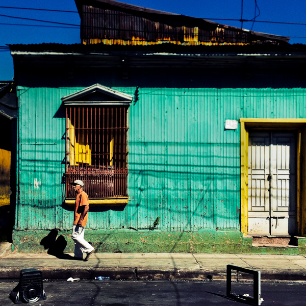 A Salvadoran man walks in front of a common lower middle class house, designed by using bold Spanish colonial architecture elements, built in a working class neighborhood of San Salvador, El Salvador.