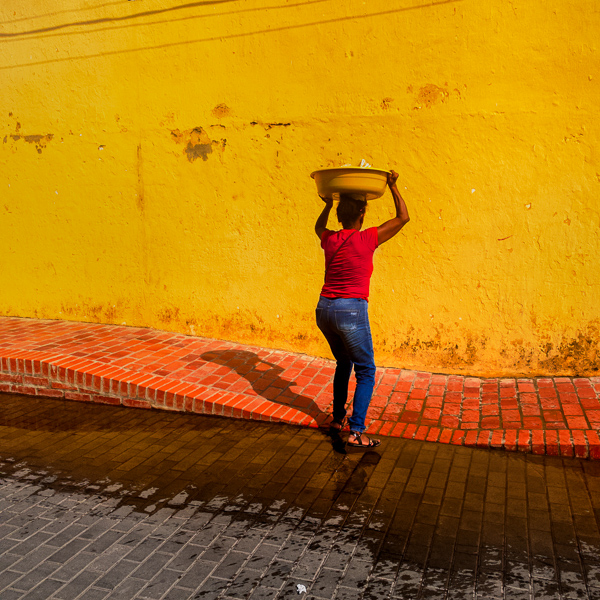 An Afro-Colombian street vendor, carrying homemade food for sale on her head, walks on the street of Santa Cruz de Mompox, Colombia.