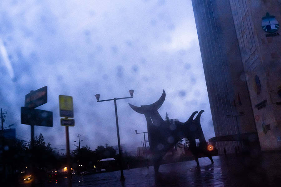 A statue of the bull seen through a rainy car window during the early evening twilight in Quito, Ecuador.