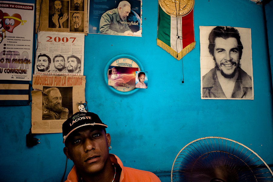 A Cuban watchmaker works in front of a wall covered by pictures of the Cuban