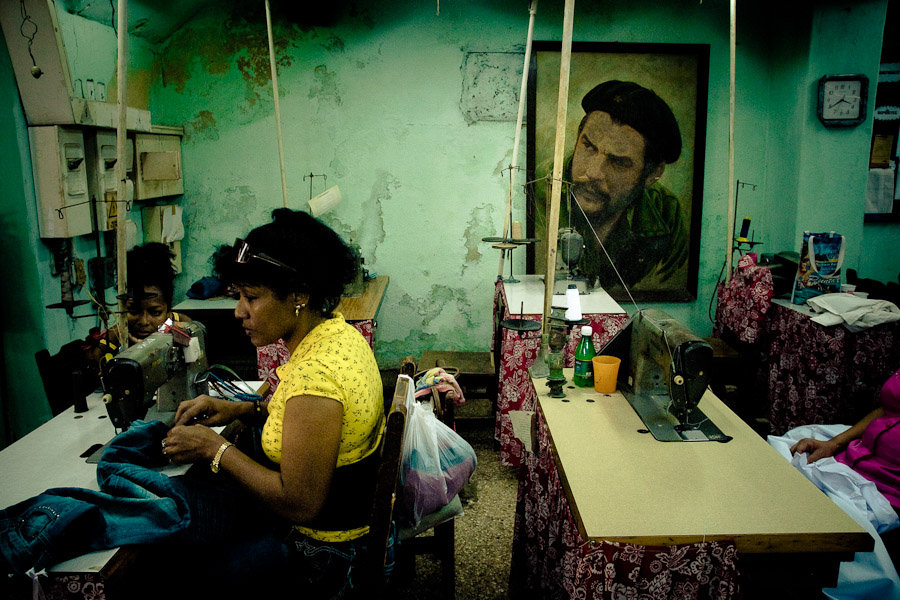 Cuban women work in front of a large portrait of the Revolutionary leader 