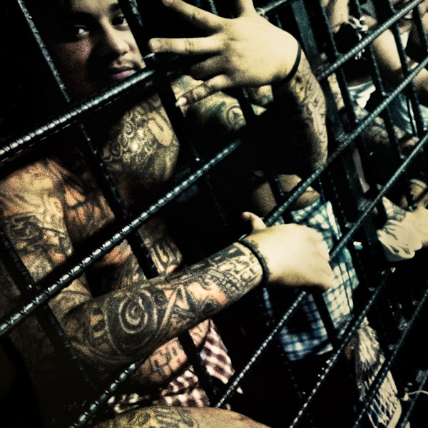 A member of the 18th Street Gang (M-18), showing the hand sign of his gang, stands behind the bars in a detention cell in San Salvador, El Salvador.