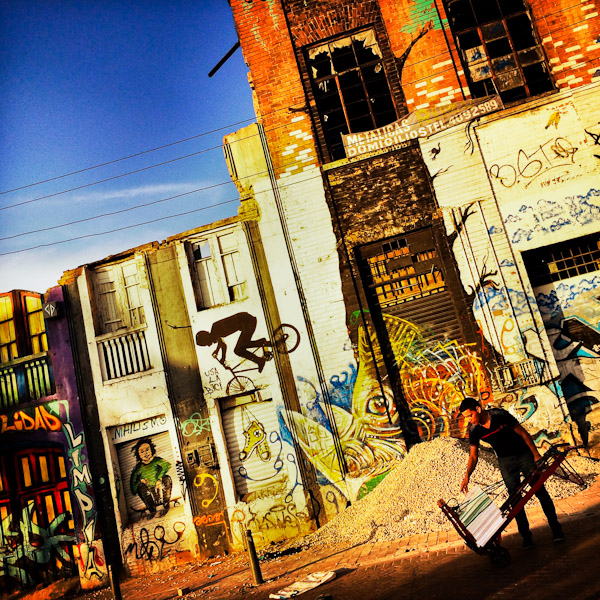 A Colombian warehouse worker transports goods in front of the abandoned factory wall, covered in painted graffiti artworks, in the center of Bogotá, Colombia.