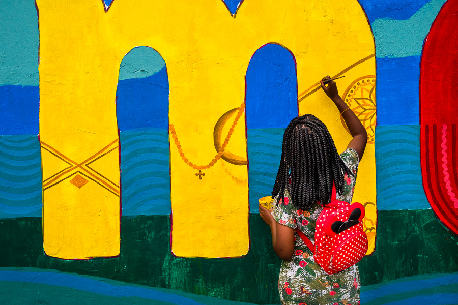 An Afro-Colombian female student paints a society and environment-related mural on a school wall in Quibdó, Colombia.