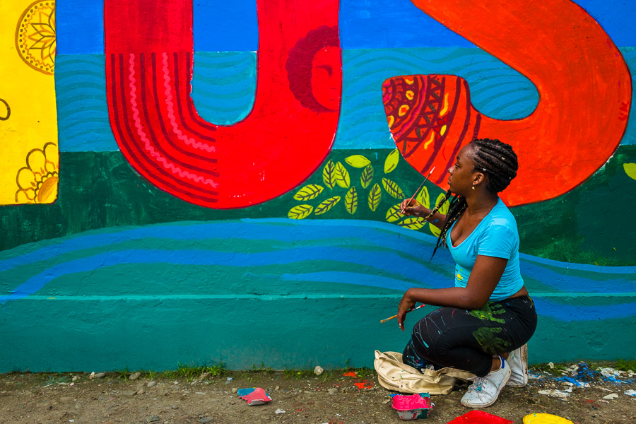 An Afro-Colombian female student paints a society and environment-related mural on a school wall in Quibdó, Colombia.