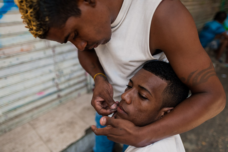 A young Colombian man shaves a friend’s beard with a razor blade in the market of Bazurto, Cartagena, Colombia.