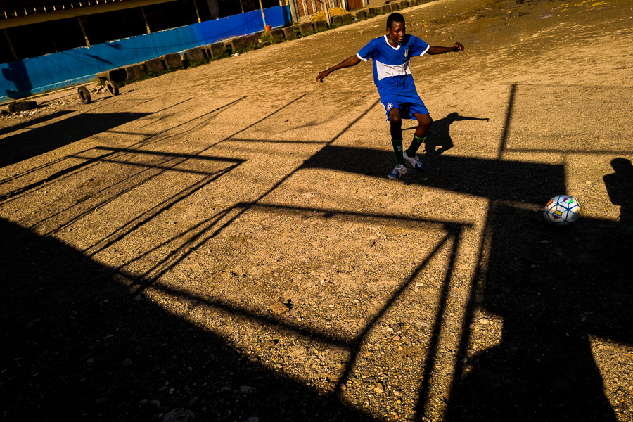 A young Afro-Colombian boy plays football during the training session on a dirt playing field in Quibdó, Chocó, Colombia.