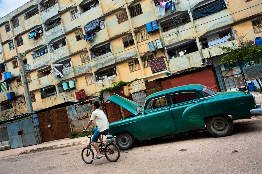 A young Cuban man rides a bicycle in front of an american classic car in Alamar, a public housing periphery in the Eastern Havana, Cuba.