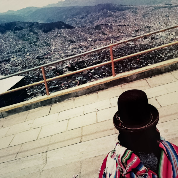 An Aymara woman, wearing the traditional bowler hat, stands on the edge of the hill in El Alto and looks down to the valley of La Paz, Bolivia.