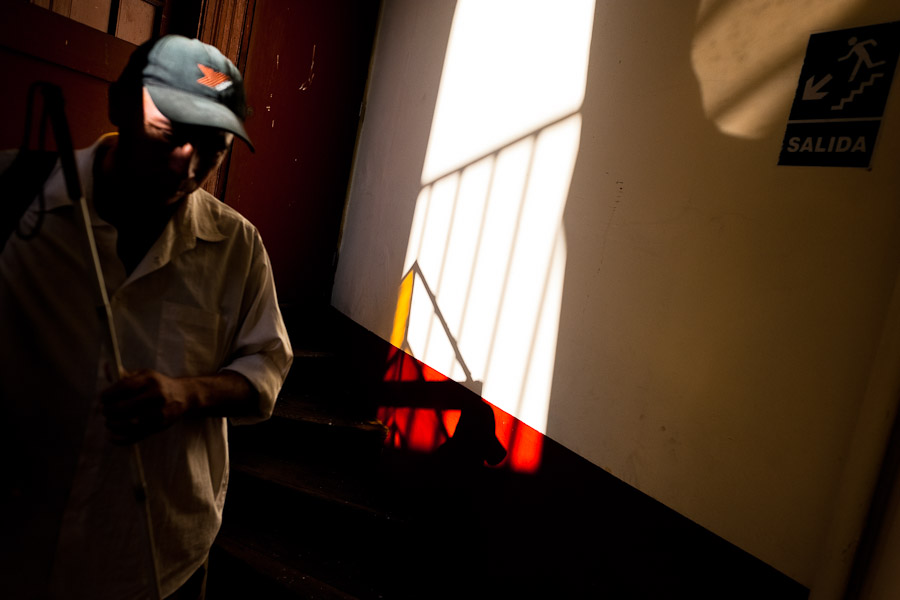 A blind man, using a white cane, finds his way in the corridor of Unión Nacional de Ciegos del Perú, a social club for the visually impaired in Lima, Peru.