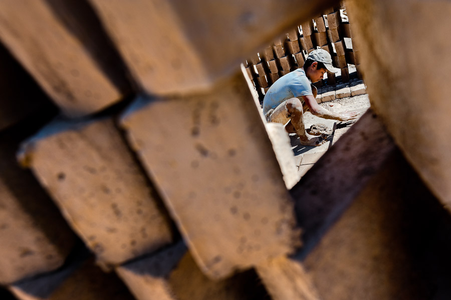 Moisés, a thirteen-year-old Salvadoran boy, is seen working behind a wall of raw bricks at a brick factory in Istahua, El Salvador.