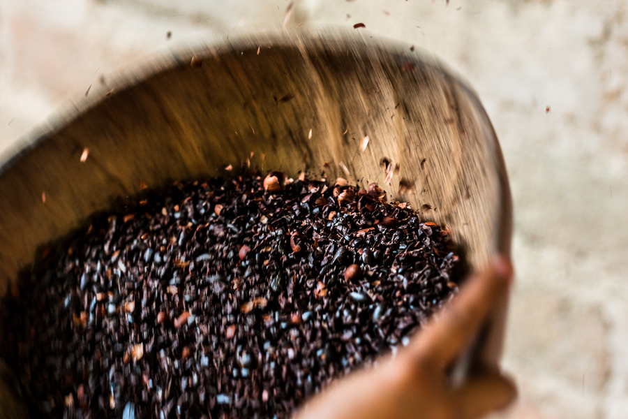 An Amuzgo indigenous woman shakes a winnowing bowl, tossing the crushed cacao beans into the air and catching them as they fall back to separate lighter outer shells from the cacao seeds, in artisanal chocolate manufacture in Xochistlahuaca, Guerrero, Mexico.