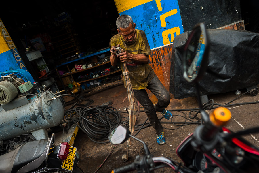 A Colombian car mechanic works on truck leaf springs in a car repair shop in Barrio Triste, Medellín, Colombia.