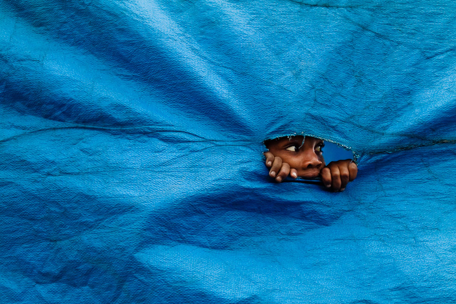 A Brazilian boy looks through the hole in a blue sheet to see unfinished allegorical floats in the Carnival workshop, Rio de Janeiro, Brazil.