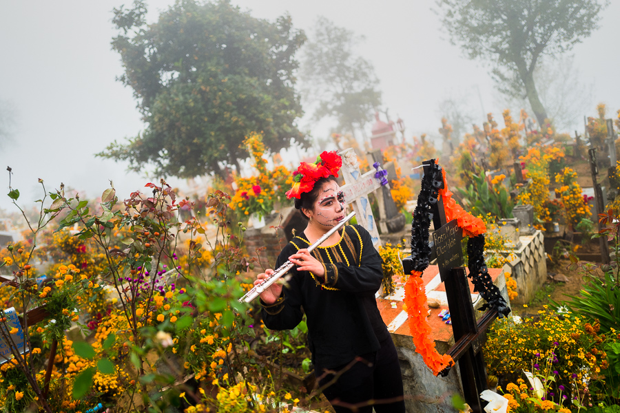 A young Mexican woman, dressed as La Catrina, plays a flute at a cemetery during the Day of the Dead celebrations in Ayutla, Mexico.