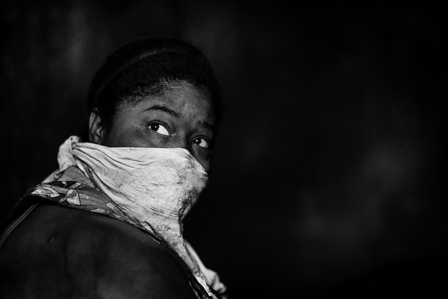 An Afro-Colombian woman, having her face covered against charcoal dust, fills plastic bags with charcoal in a charcoal storage room in Cartagena, Colombia.