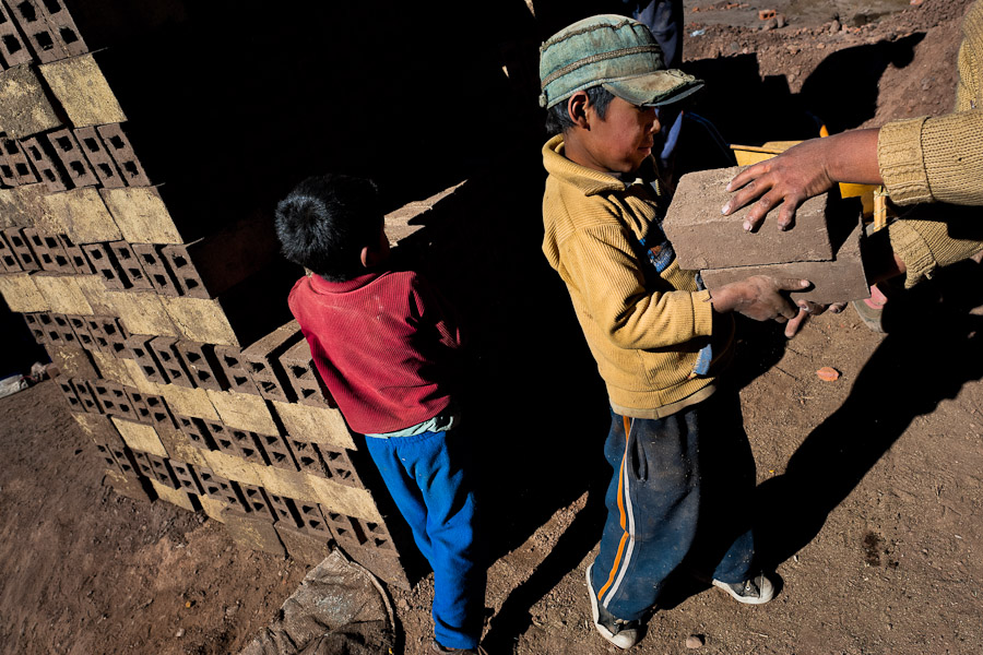 Peruvian boys, working with their parents, load raw bricks at a brick factory in the outskirts of Puno, Peru.