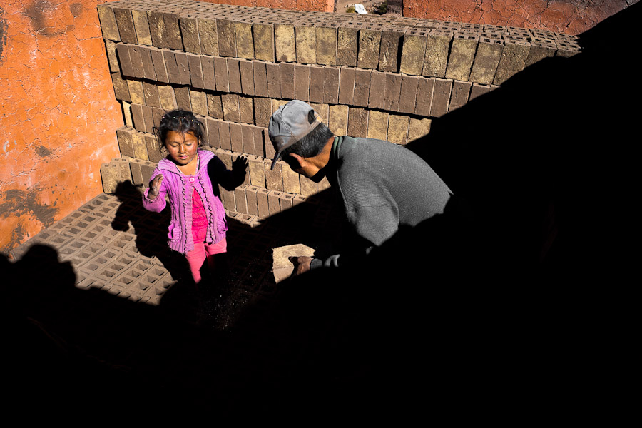 A Peruvian girl, working with her father, piles raw bricks inside a kiln at a brick factory in the outskirts of Puno, Peru.