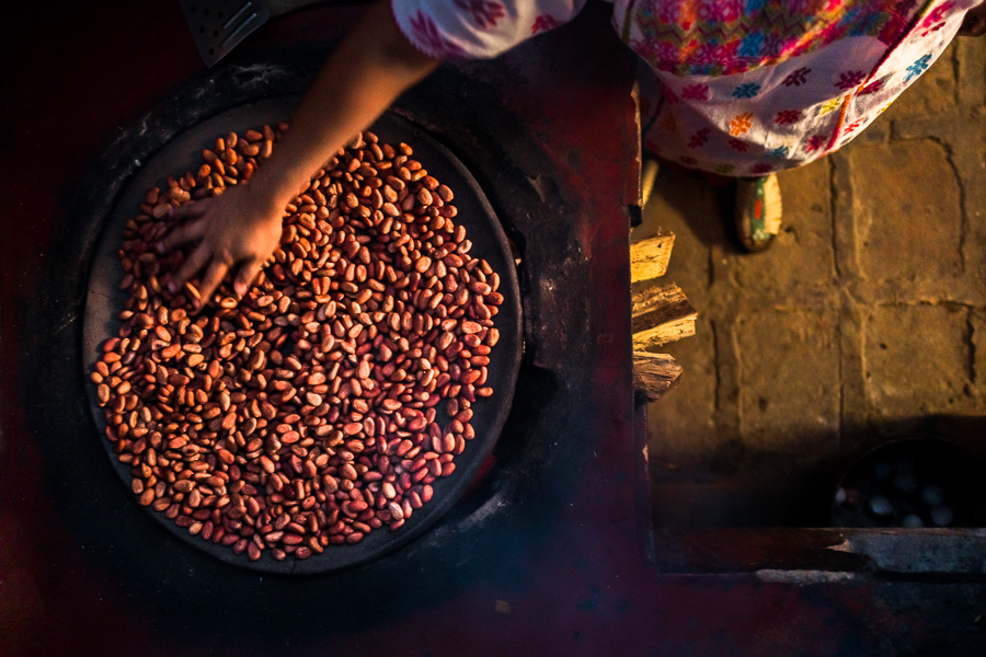 An Amuzgo indigenous woman roasts cacao beans on a clay plate over fire in artisanal chocolate manufacture in Xochistlahuaca, Guerrero, Mexico.