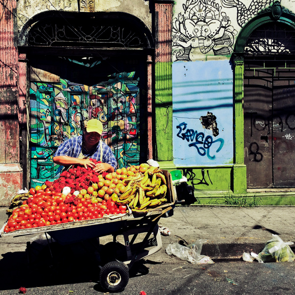A Salvadoran man sells fruits in front of a ruined house with Spanish colonial architecture elements, painted over by a local artist, in the center of San Salvador, El Salvador.