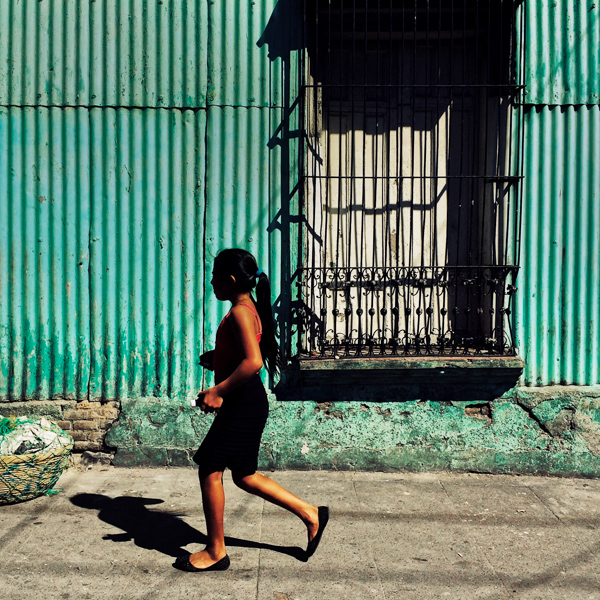 A Salvadoran girl walks in front of a common lower middle class house, designed by using bold Spanish colonial architecture elements, built in a working class neighborhood of San Salvador, El Salvador.