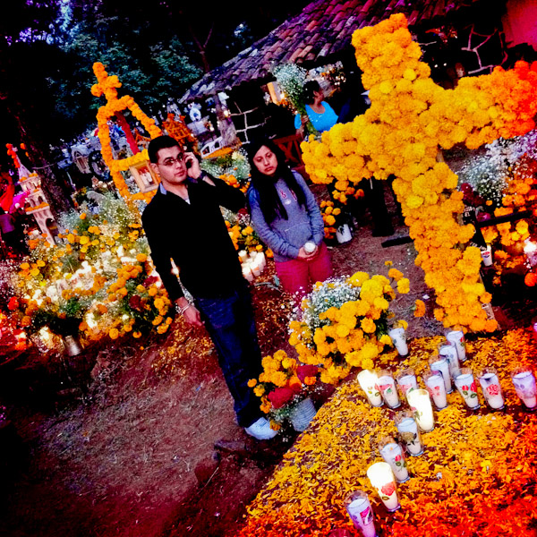 A Mexican couple stands next to a grave, covered by marigold flowers, honouring their deceased relatives during the ritual celebration of the Day of the Dead (Día de Muertos) at the cemetery of Tzintzuntzan, Michoacán, Mexico.