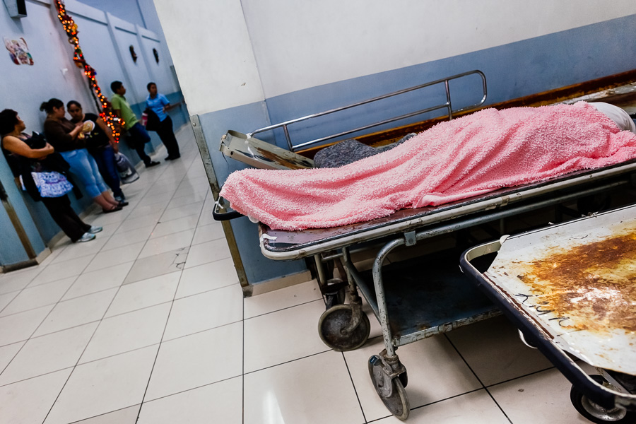 A dead body of a deceased patient, covered by a bath towel, lies on the strecher in the corridor inside the emergency department of a public hospital in San Salvador, El Salvador.