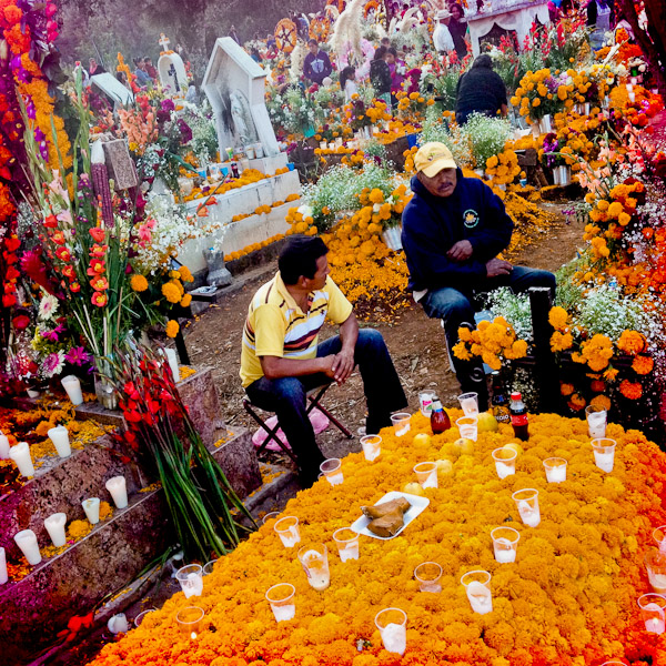 Mexican men sit around a grave, covered by marigold flowers, honouring their deceased relatives during the ritual celebration of the Day of the Dead (Día de Muertos) at the cemetery of Tzurumútaro, Michoacán, Mexico.