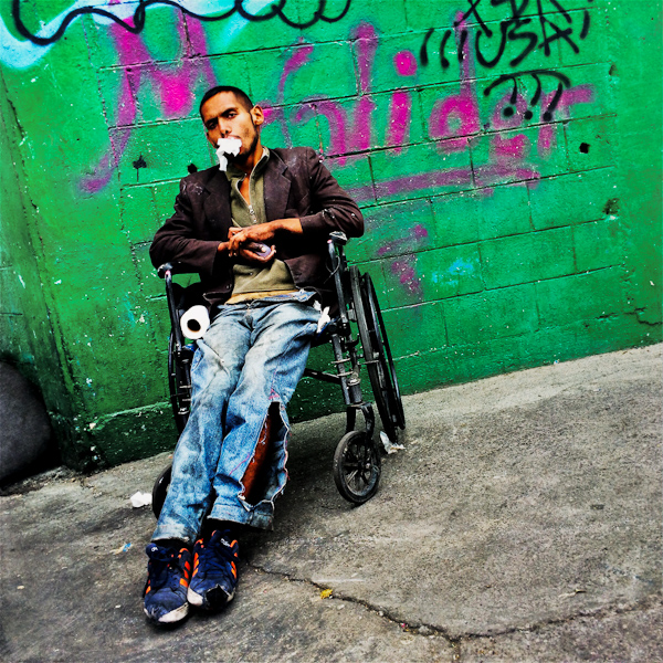 A young drug addict inhales a color solvent through his mouth, while sitting on a wheel chair in the street of Mexico City, Mexico.