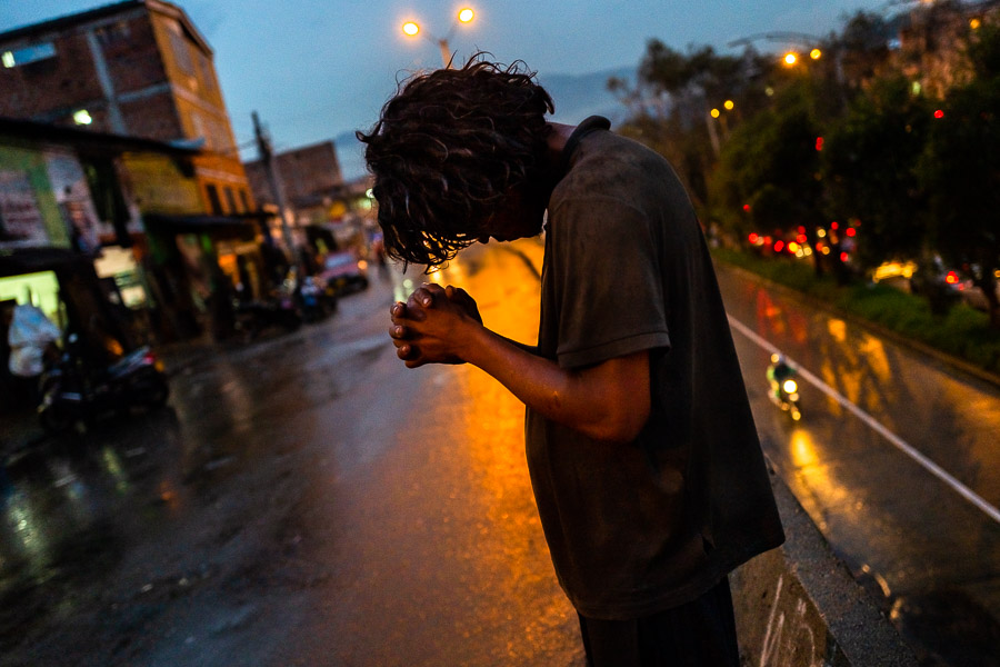 A Colombian man, having his hands clasped in a heavy intoxication of “bazuco”, stands along the city road in Medellín, Colombia.