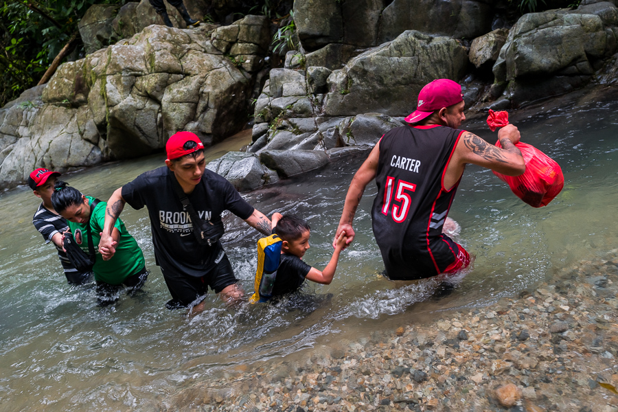 An Ecuadorian migrant family, helping each other, wades through the river in the wild and dangerous jungle of the Darién Gap between Colombia and Panamá.