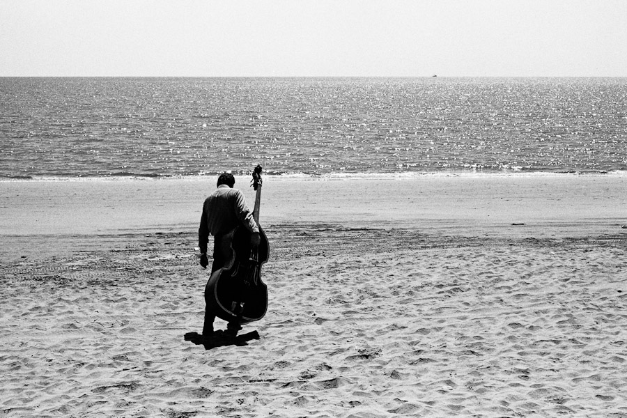 A Mariachi player carries his contrabass on the beach in Mexico.