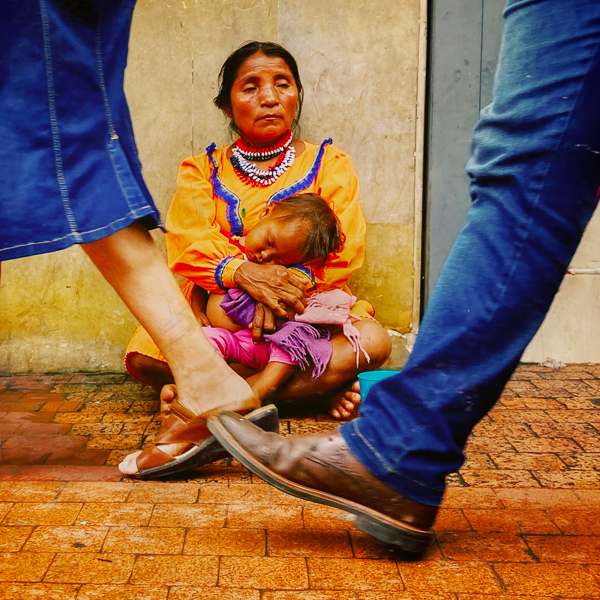 An Embera Chamí indigenous woman with a child begs for alms while Colombians passing by in the street in Cali, Colombia.