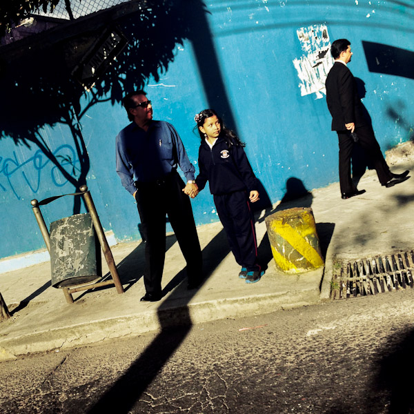 An Ecuadorian man, holding his daughter's hand, walks across the street during the sunny afternoon in Quito, Ecuador.