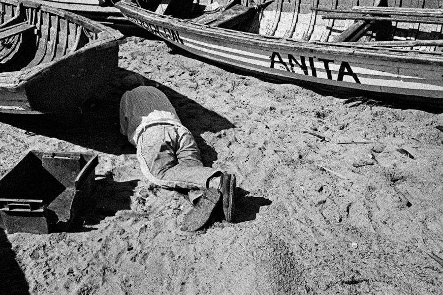 A Chilean fisherman, after drinking a couple of pisco shots, rests in the shadow of his boat on the beach of Quintero, Chile.