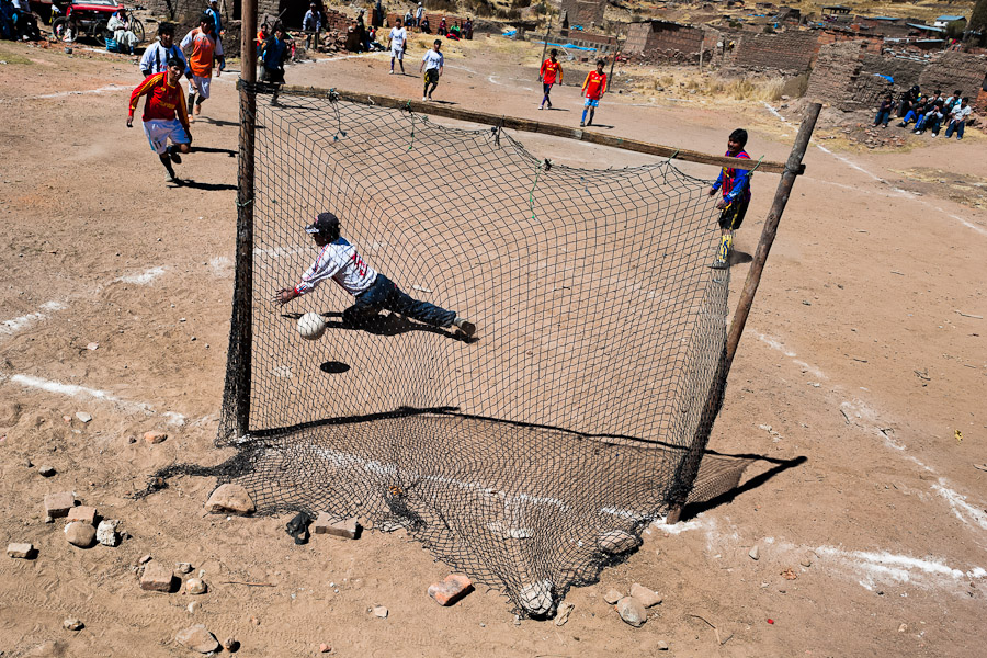 Indigenous men play football on a dusty football pitch in the rural mountain community close to Puno, Peru.