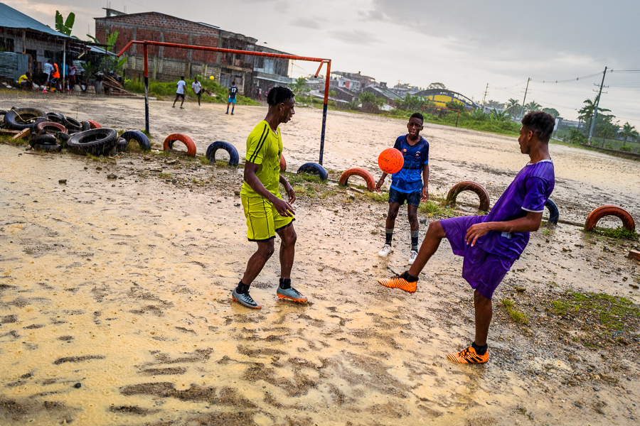 Young Afro-Colombian men play football in a tropical rain storm while performing daily training in Quibdó, Colombia.