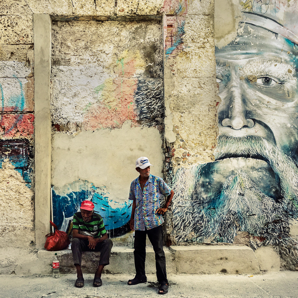 Old Colombian men sit bellow a large mural in the street of Getsemaní, a popular artistic neighborhood in Cartagena, Colombia.