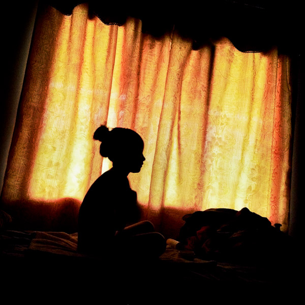 A young girl sits in front of a curtained window in Mindo, Ecuador.