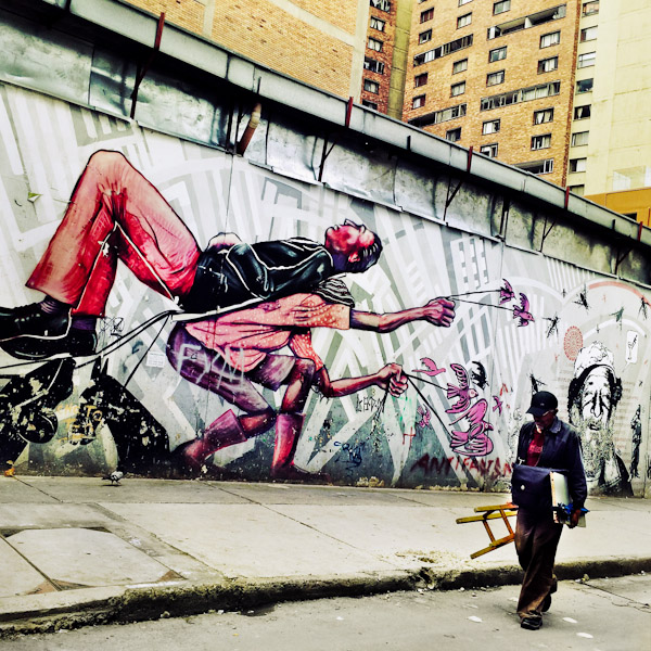 A Colombian street painter passes in front of a graffiti artwork, depicting the equality & liberation themes, created by an artist named Guache in the center of Bogotá, Colombia.