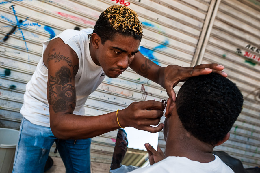 A young Colombian man shaves a friend’s beard with a razor blade in the market of Bazurto, Cartagena, Colombia.