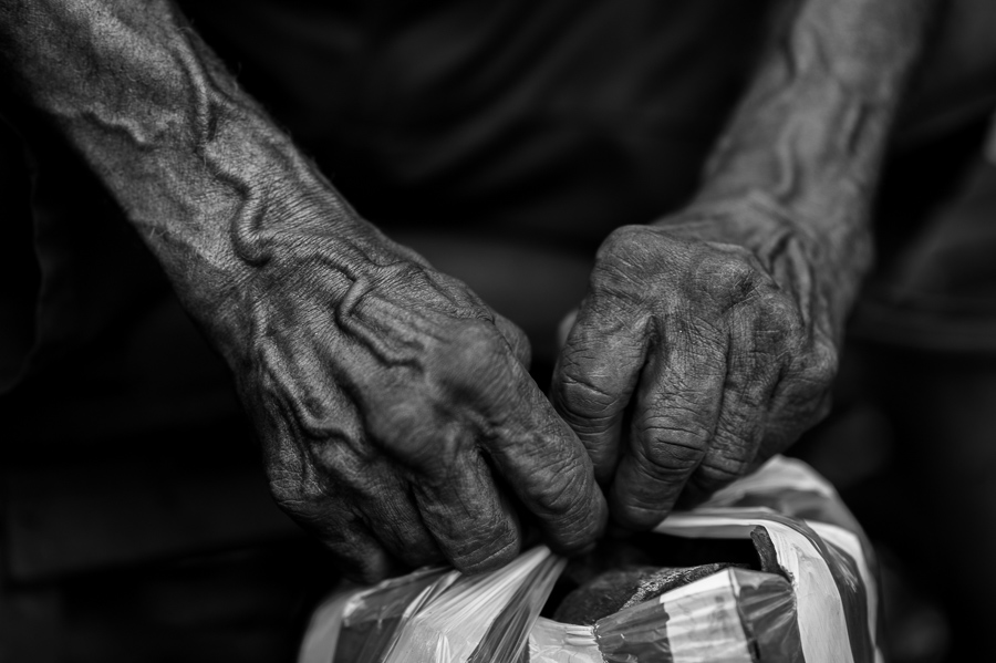 Hands of an Afro-Colombian charcoal worker, full of bulging veins, are seen tying a plastic bag filled with charcoal for sale in a street market in Barranquilla, Colombia.