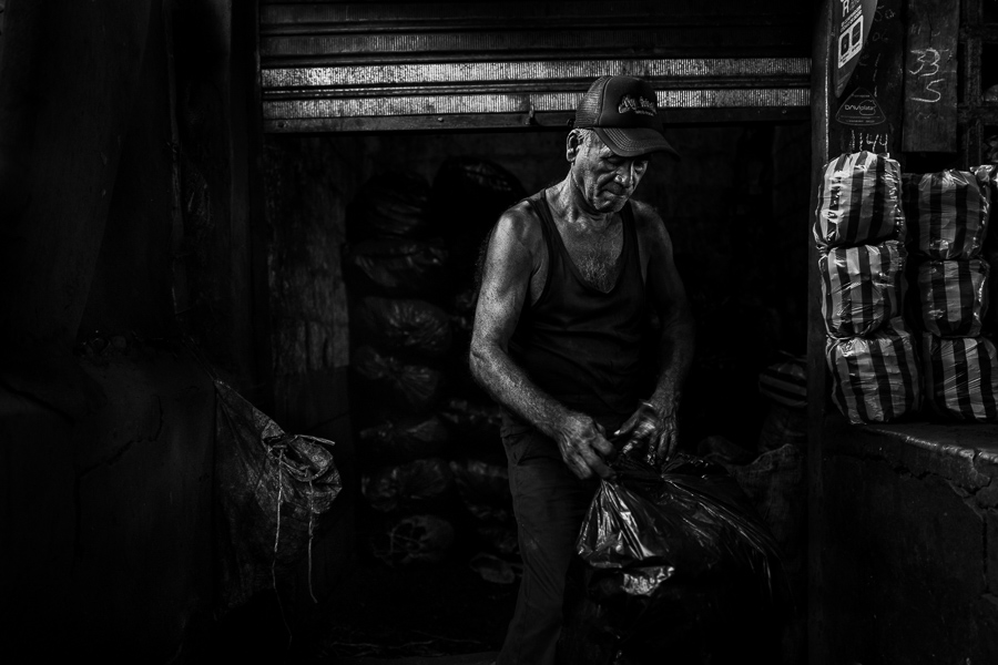 A Colombian charcoal worker fills plastic bags with charcoal in front of a rented storage room in the street market in Barranquilla, Colombia.