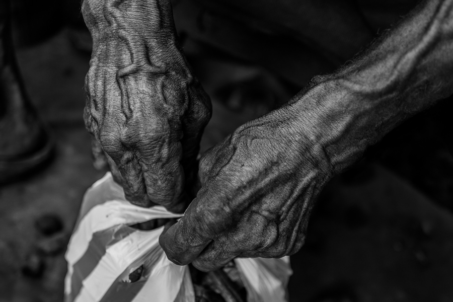 Hands of an Afro-Colombian charcoal worker, full of bulging veins, are seen tying a plastic bag filled with charcoal for sale in a street market in Barranquilla, Colombia.