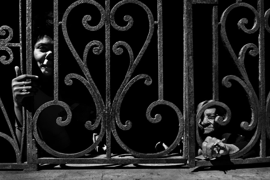 Cuban women seen in the shadow behind the window grill during a hot afternoon in Havana, Cuba.